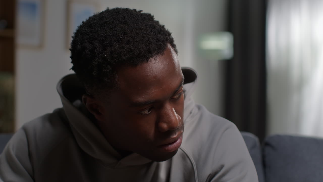 Close Up Of Unhappy And Depressed Young Man With Head In Hands Sitting On Sofa At Home Shaking Head