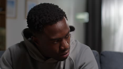 close up of unhappy and depressed young man with head in hands sitting on sofa at home shaking head