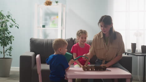 toddler boy waters seeds in tray with mother and sister