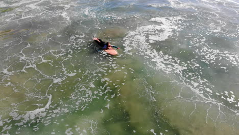 la solitaria chica surfista jo snider, un dron aéreo de 4k sigue mientras rema a través de las olas para esperar a uno en la competencia de surf del muelle de la playa de huntington, océano pacífico