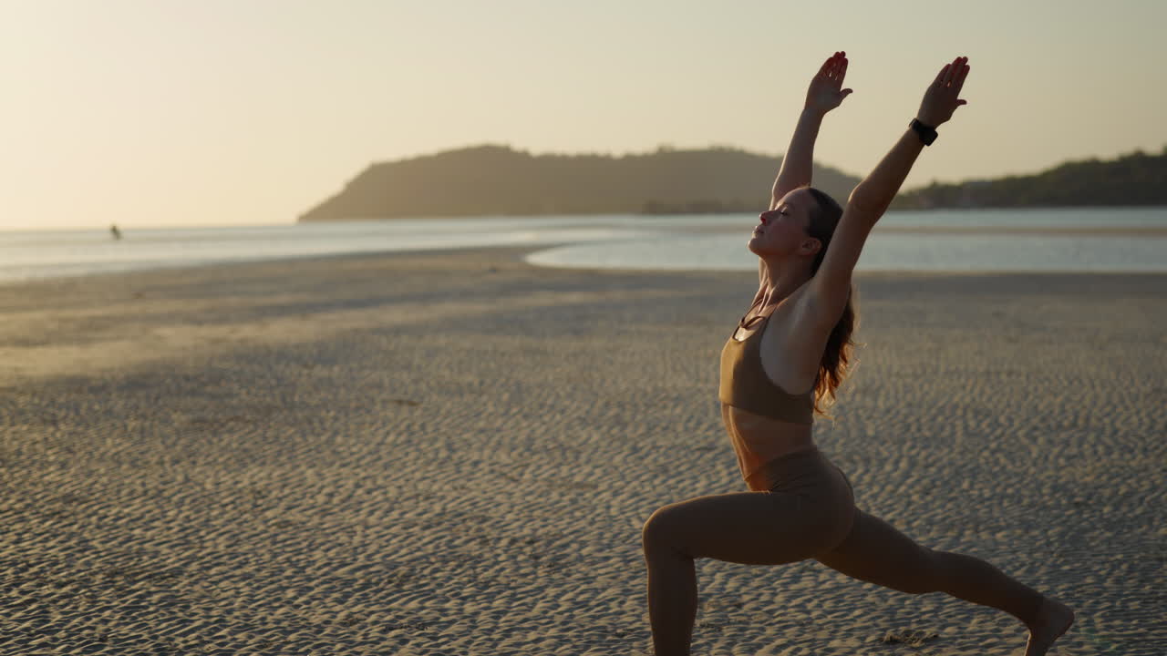 Donna che pratica la Posizione del Guerriero Yoga su una spiaggia sabbiosa al tramonto