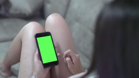 mujeres jóvenes asiáticas acostadas en el sofá y usando teléfono inteligente con pantalla verde en la sala de estar.