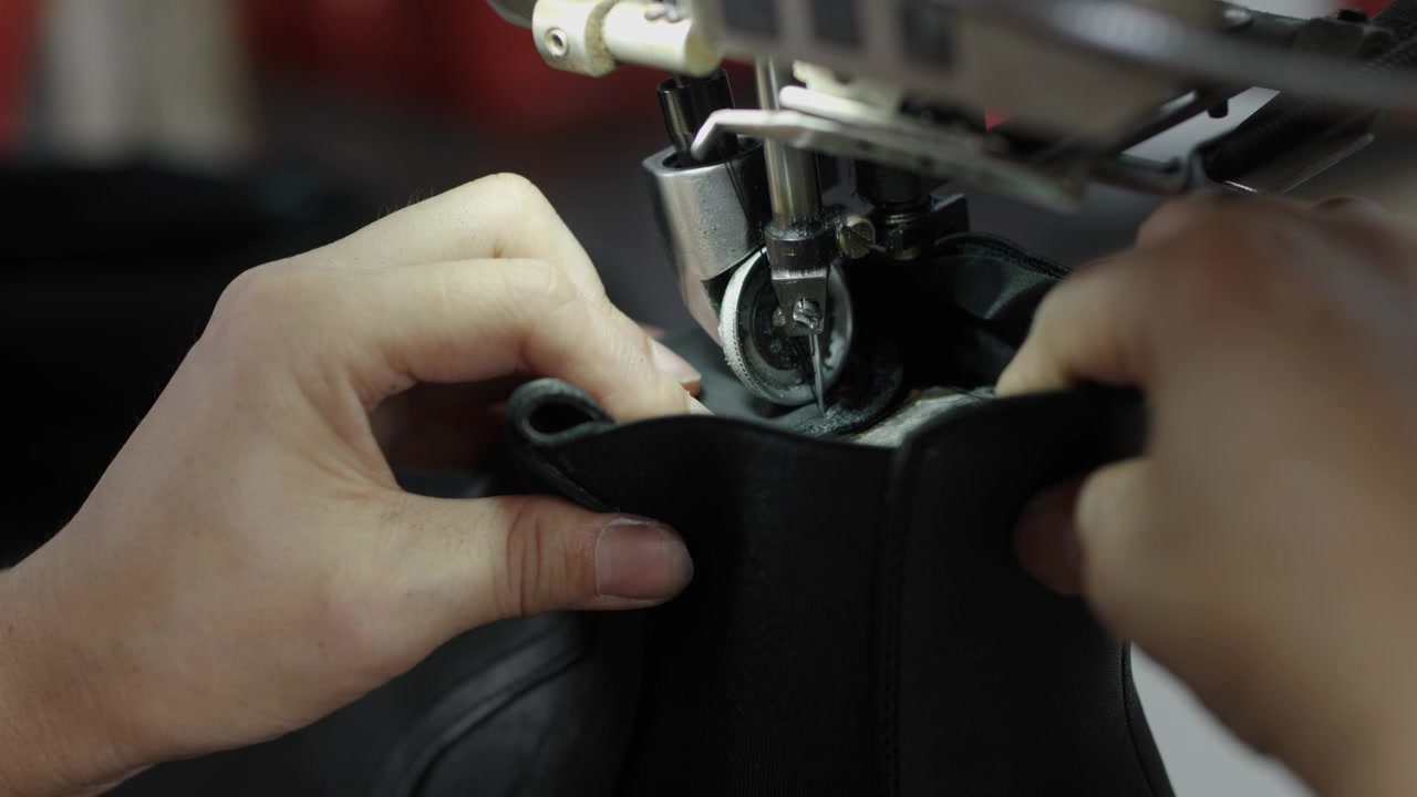 Hands sewing black shoe upper with industrial machine in workshop closeup