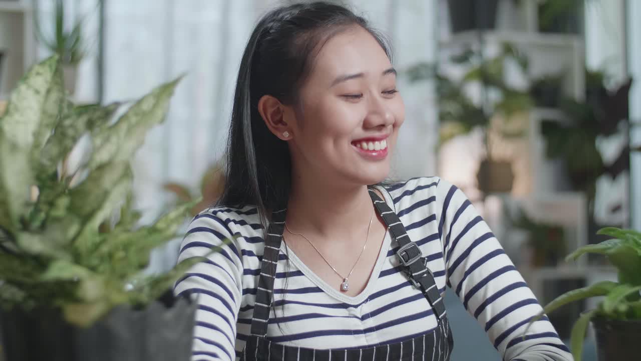 식물과 함께 아시아 여성의 클로즈업 그녀의 팔을 교차하고 집에서 카메라에 미소