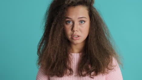 caucasian curly haired woman keeping finger over lips in front of the camera.