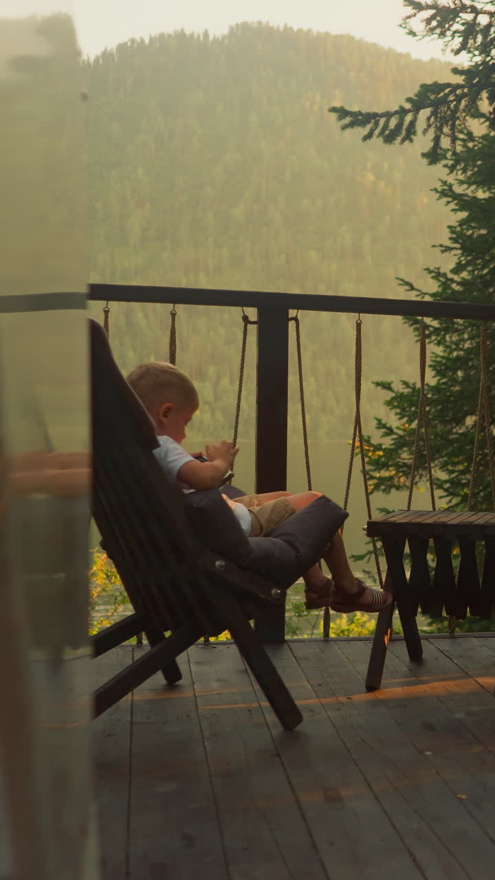 niños encantadores con cabello claro se sientan en sillas disfrutando de juegos móviles en teléfonos celulares contemporáneos. niños pequeños pasan tiempo contra el paisaje con bosque nebuloso