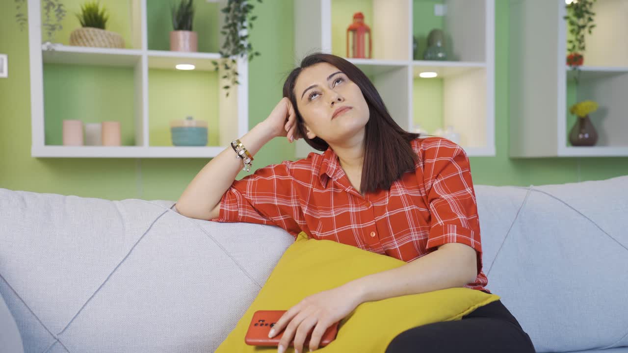 自宅で無力そうに携帯電話を見ている不幸せな若い女性