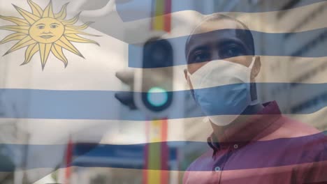 Animation-of-flag-of-uruguay-waving-over-man-wearing-face-mask-during-covid-19-pandemic