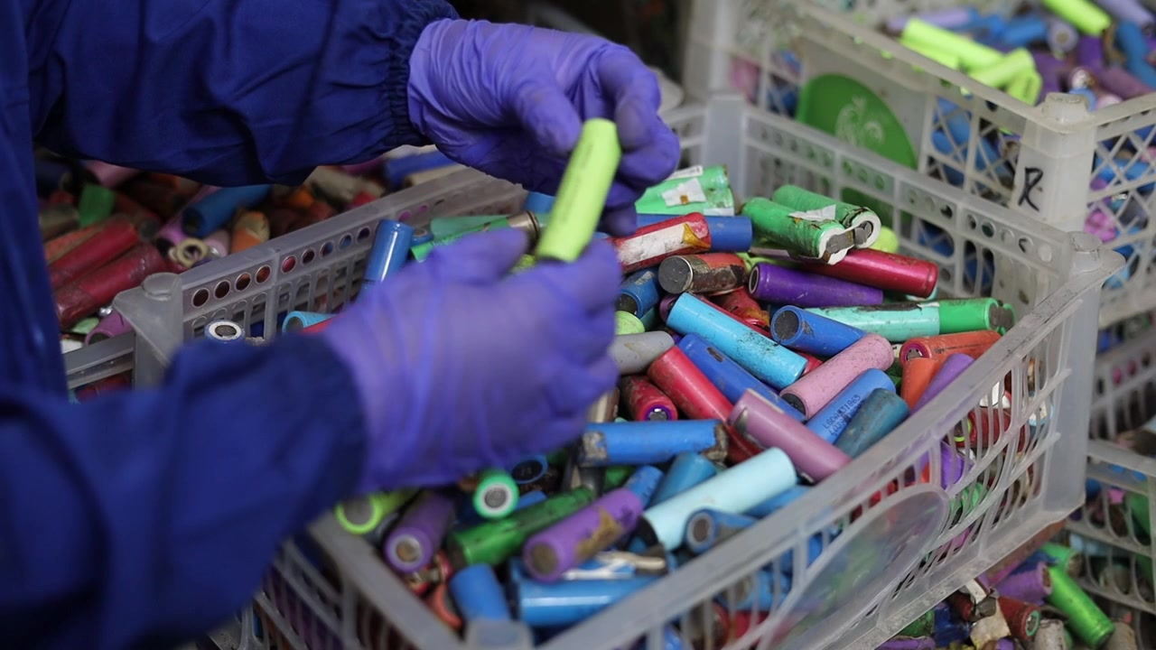 A worker wearing protective gloves sorts used lithium batteries in a recycling facility, separating different battery cells for proper handling and sustainable recycling.