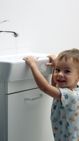 smiling child standing at the sink open the tap. happy baby learns to use the faucet. vertical video