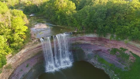 aerial footage of flowing balls falls waterfall into a deep green pool of water