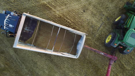 Grain-being-unloaded-from-truck-using-a-tractor-driven-auger,-top-aerial-view