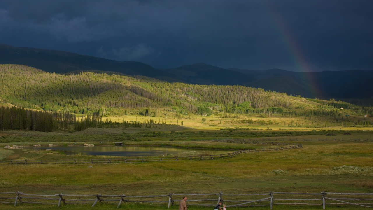 nubes grises oscuras y un colorido arco iris sobre una exuberante montaña verde en un clima tormentoso