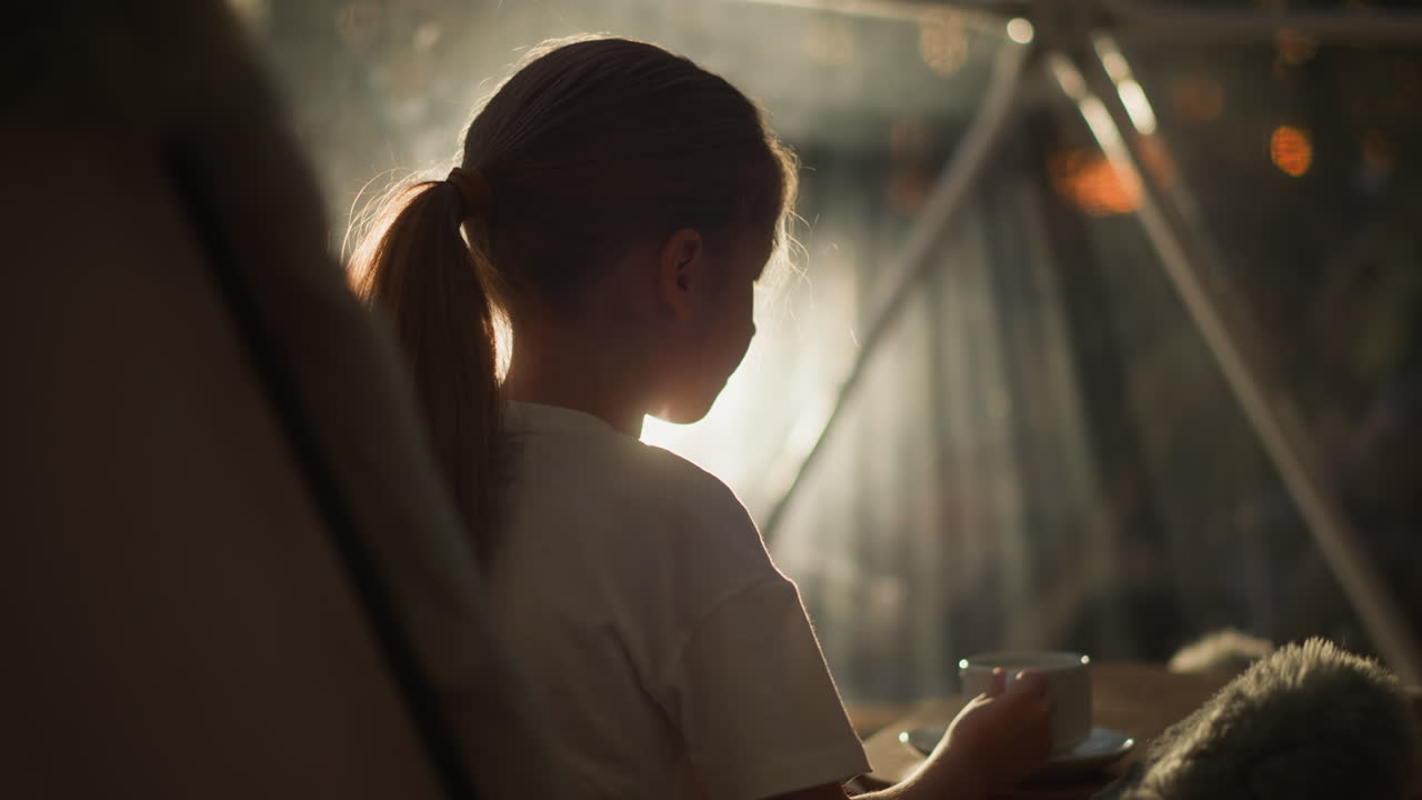 아이는 빛 창문 앞에서 차를 마시고, 귀여운 소녀는 쾌적한 핑 텐트에 앉아 달한 음료를 즐기고, 편안한 아이는 집에서 빛 아침을 보낸다.