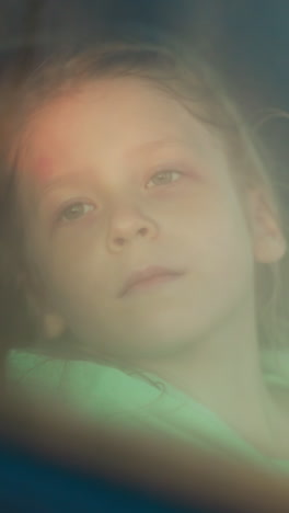 thoughtful child looks at waterdrops sitting in car. pensive little girl contemplates rain sprays on auto window at riding. travelling by taxi on stormy day