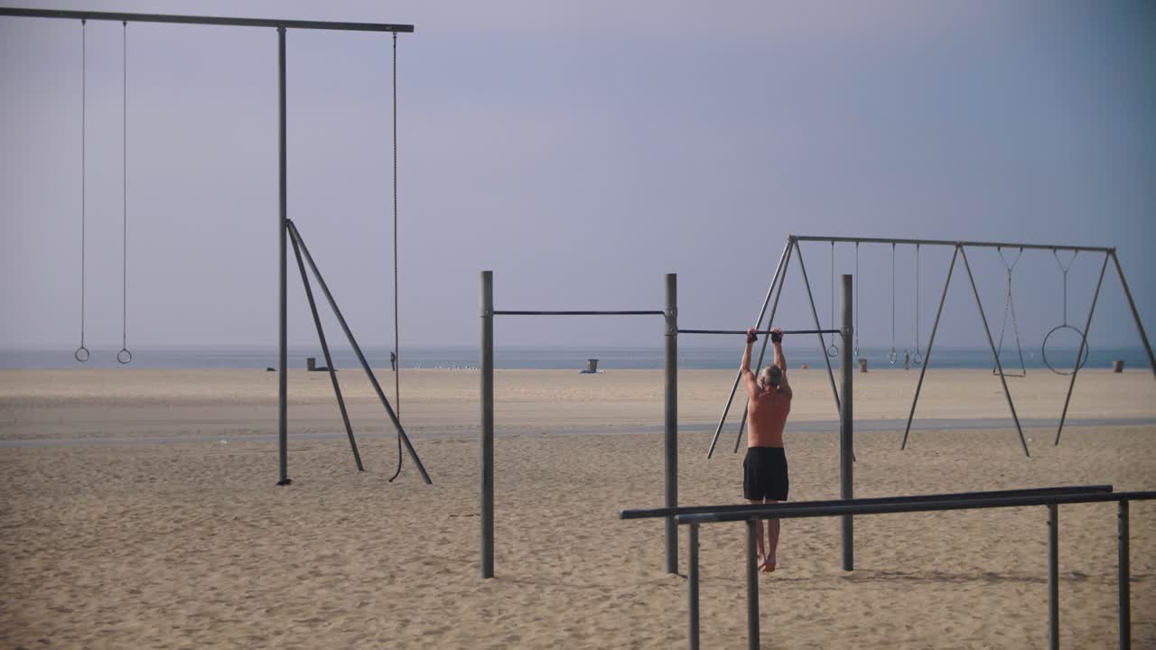 imágenes en cámara lenta de 4k de un hombre haciendo ejercicio en un parque de entrenamiento en una playa - hombre haciendo dominadas al aire libre - parque muscular - playa de venice - santa monica los angeles