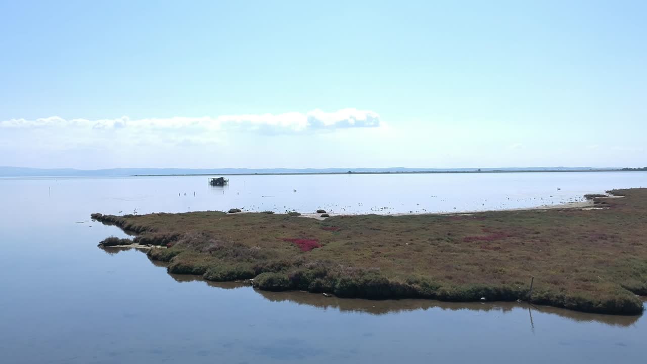 Forward moving drone shot over a patch of land towards a fishing shack in the ocean close to Axios river in Thessaloniki-Northern Greece