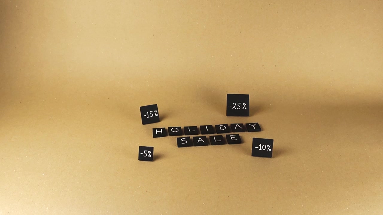 Sorte fliser, der staver "holiday sale", omgivet af roterende rabatprocenttegn på en neutral brun papirbaggrund. En konceptuel video til detailmarkedsføring, sæsonbestemte kampagner og shopping.