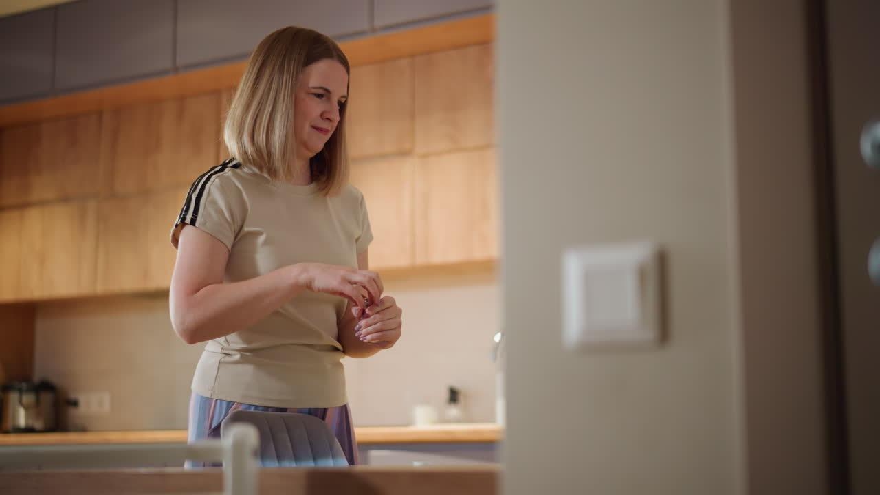 Woman standing near kitchen table holding small container looking at pink aquarium with colorful fish, green plants, decorative rocks, and glowing light creating calm domestic atmosphere inside modern home