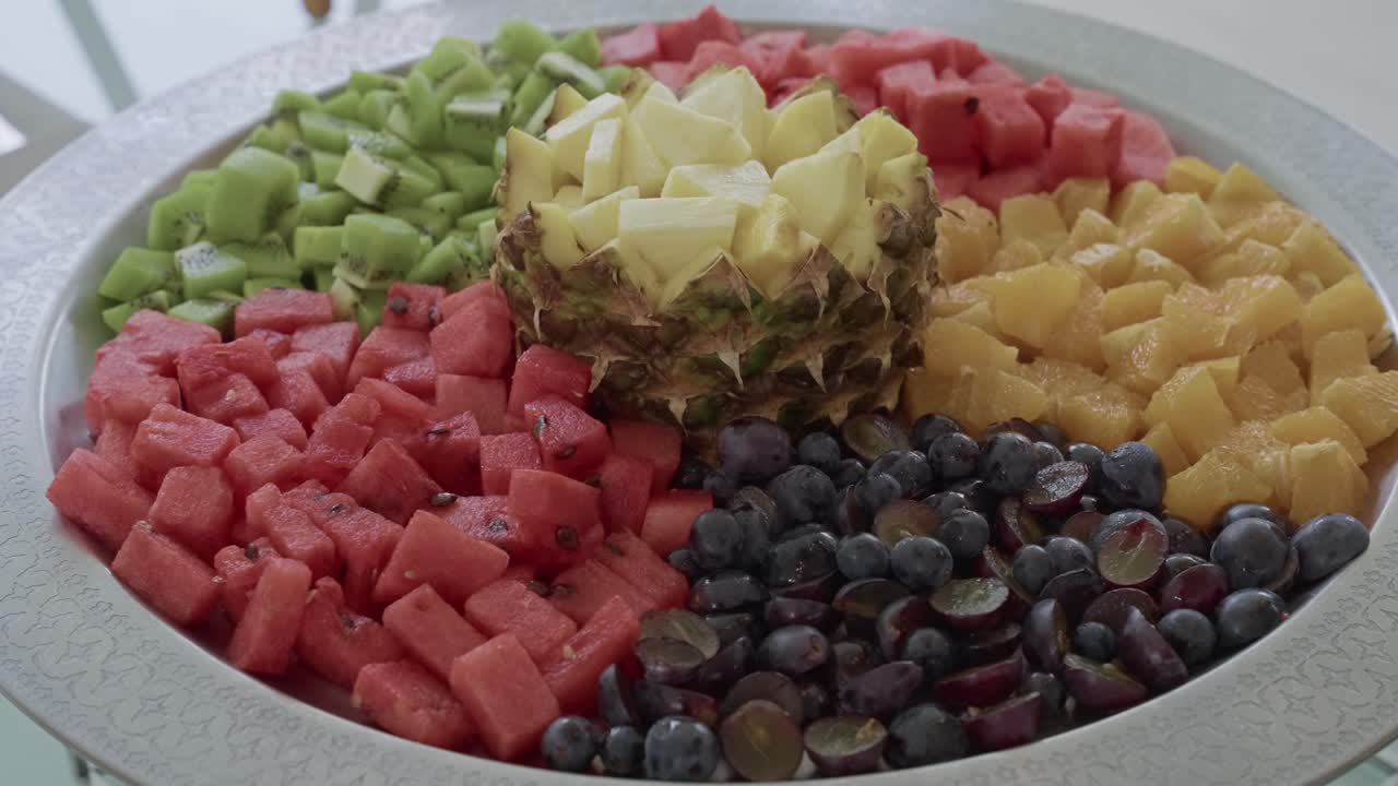 kiwi, sandía, piña, uvas y naranja recién cortados dispuestos en una vibrante bandeja circular de fruta