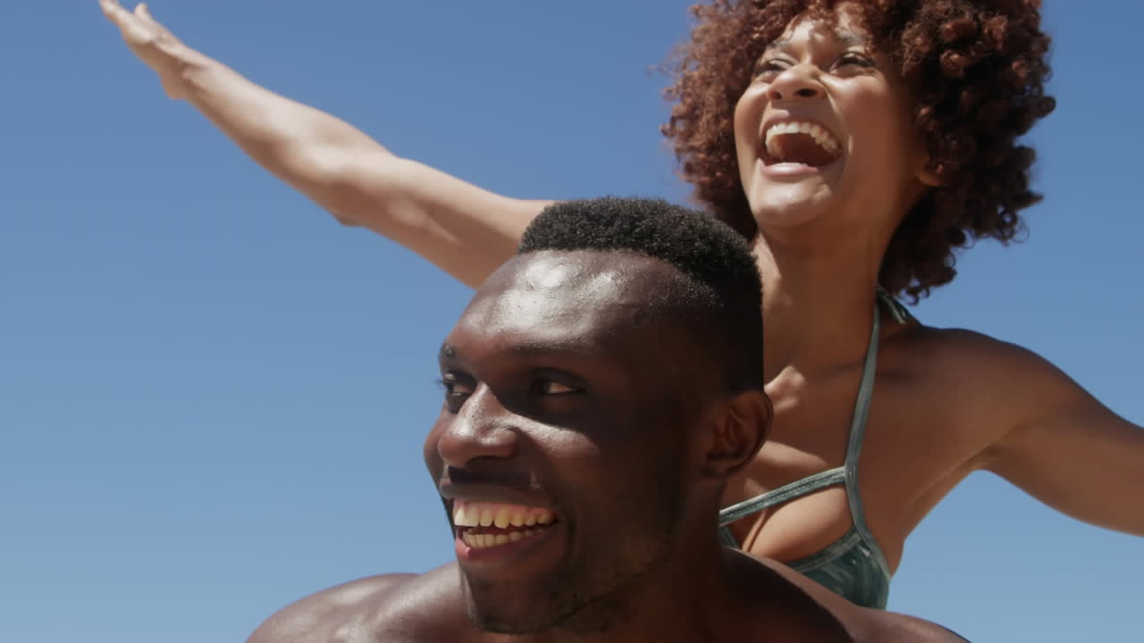 Formes abstraites sur un texte "vibes" au-dessus d'un homme afro-américain portant sa femme sur son dos à la plage