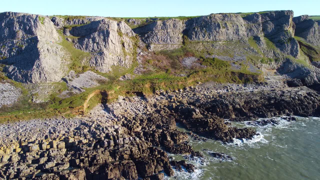 Aerial Overview Along Welsh Coastline with Eroding Grass Banks and Rock Formations with Coastal Path at Top. Beautiful Gower Peninsula Tourist Destination
