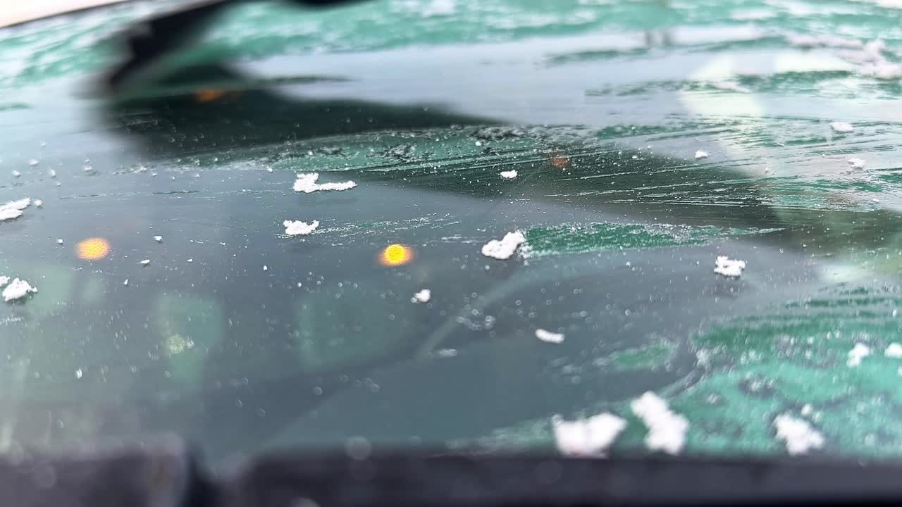 Il ghiaccio ricopre il parabrezza di un'auto al mattino. Una persona raschia il ghiaccio per una visuale migliore e più sicura