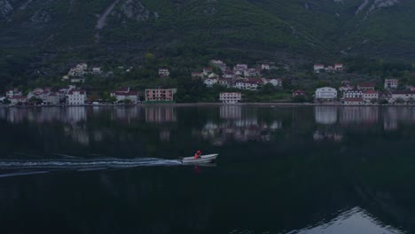 Orbit-around-local-fishermen-in-small-boat-at-Kotor-bay-with-sunrise,-aerial