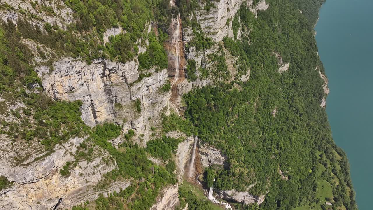 Aerial view of Seerenbachfälle waterfall cascading down Swiss cliffs near Walensee, surrounded by lush forest and blue alpine lake