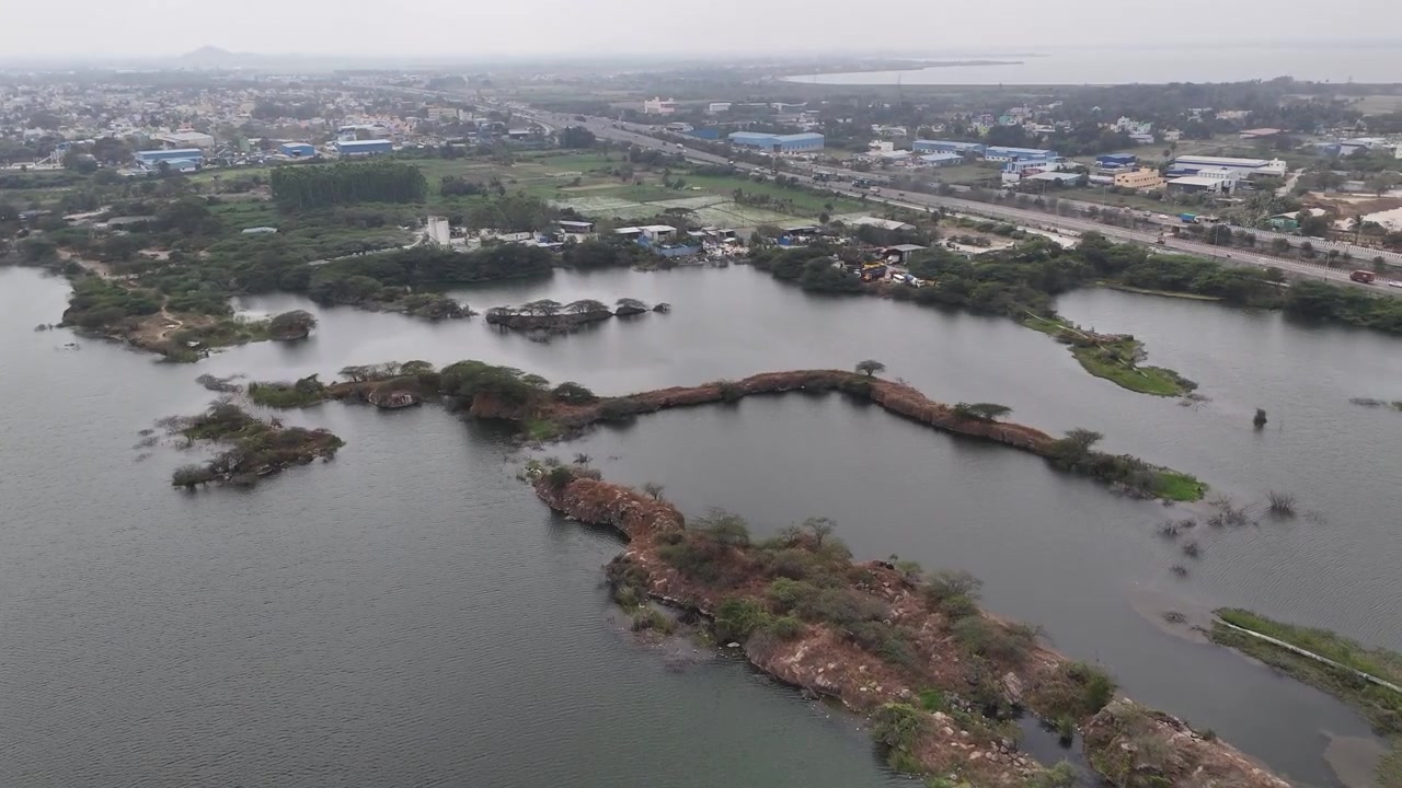 Veduta aerea cinematografica della cava di granito di Sikkarayapuram, con laghi di cava allagati, aspre isole di granito, zone umide bonificate e lo skyline distante di Chennai in un drammatico paesaggio post-minerario.