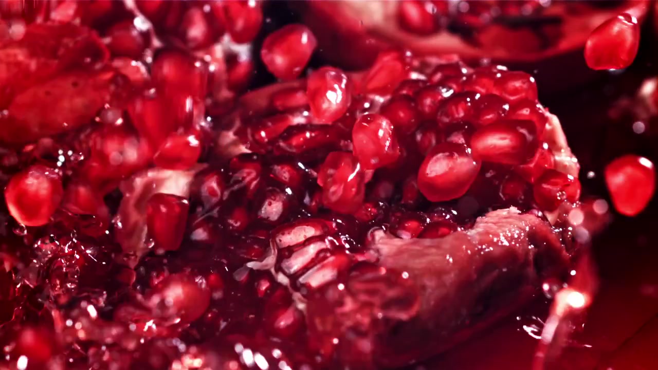 Levende røde granatæblekerner falder og plasker i slowmotion