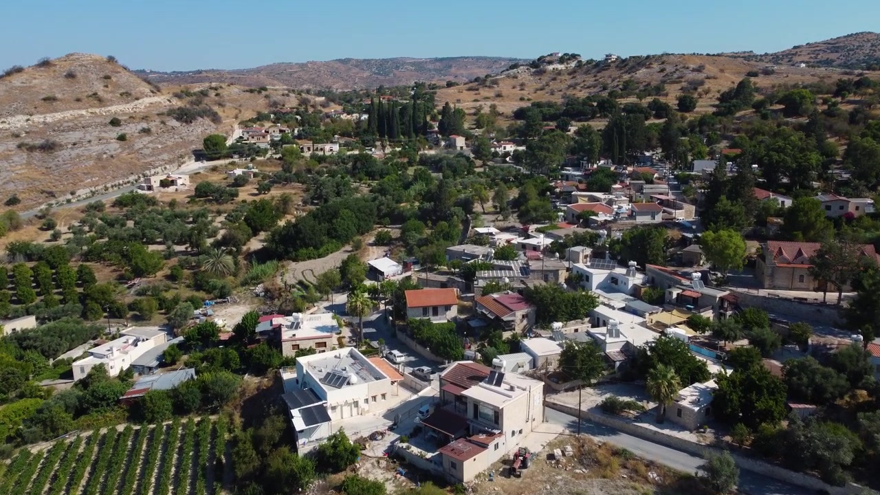 Scivolando in avanti e avvicinandosi a un tradizionale villaggio collinare e a una tenuta vinicola immersi in un paesaggio mediterraneo arido in un pomeriggio limpido e con cielo azzurro
