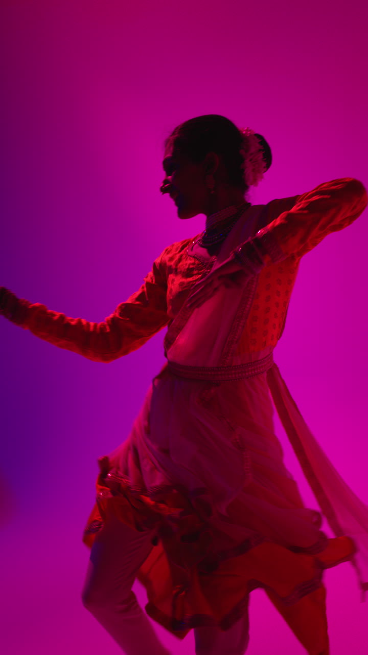 video vertical de una bailarina de kathak giratoria realizando un baile vestida con el vestido tradicional indio contra un fondo púrpura 2