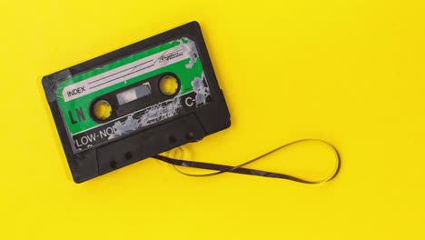 old-retro-cassette-tape-with-grunge-label-rewinding-pulled-tape-on-yellow-background-stop-motion