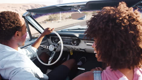 young black couple driving open top car on a desert highway