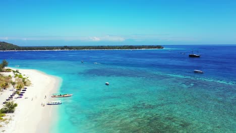 Paradiesische-Tropische-Bucht-Mit-Weißem-Sandstrand-Und-Blau-türkisfarbener,-Ruhiger-Lagune,-In-Der-Boote-In-Einem-Hellen-Himmel-über-Einer-Tief-Liegenden-Insel-In-Indonesien-Schwimmen