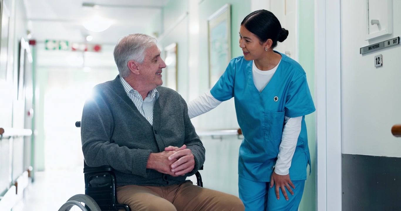 Nurse Talking to Senior Man in Wheelchair in Hospital Corridor