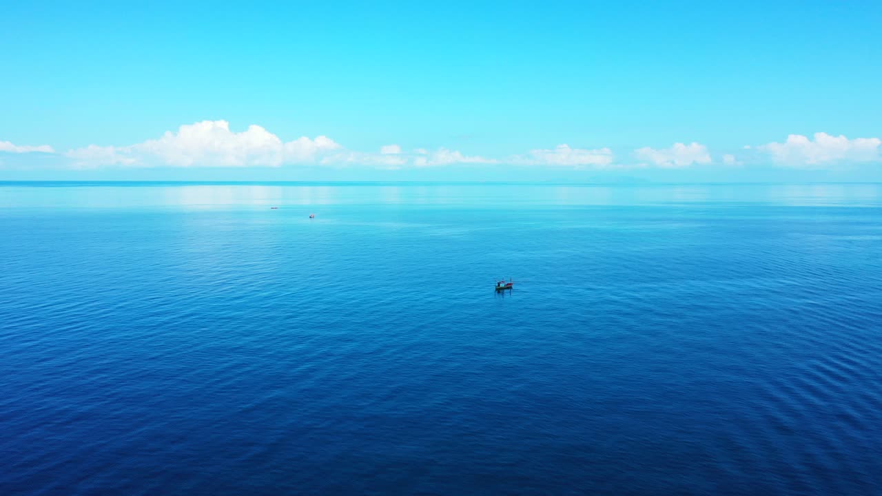 흰 구름과 밝은 하늘을 반사하는 푸른 바닷물, 인도네시아 열대 섬 해안 근처에 보트가 떠 있는 평화로운 바다 풍경