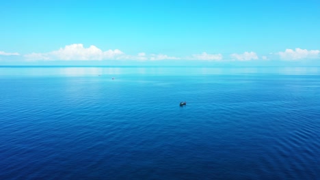 Blue-sea-water-reflecting-white-clouds-and-bright-sky,-peaceful-seascape-with-boat-floating-near-shore-of-tropical-island-in-Indonesia