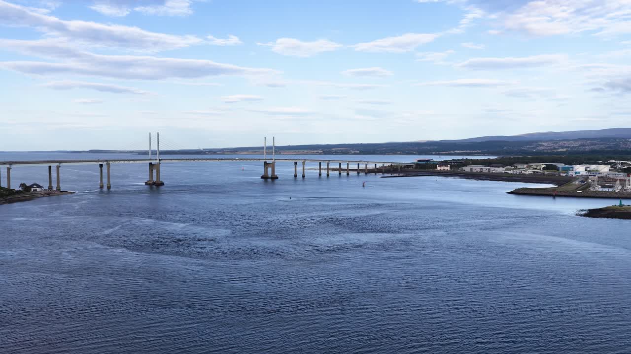 Smooth aerial pan reveals bridge, river, and waterfront under bright daylight with scattered clouds