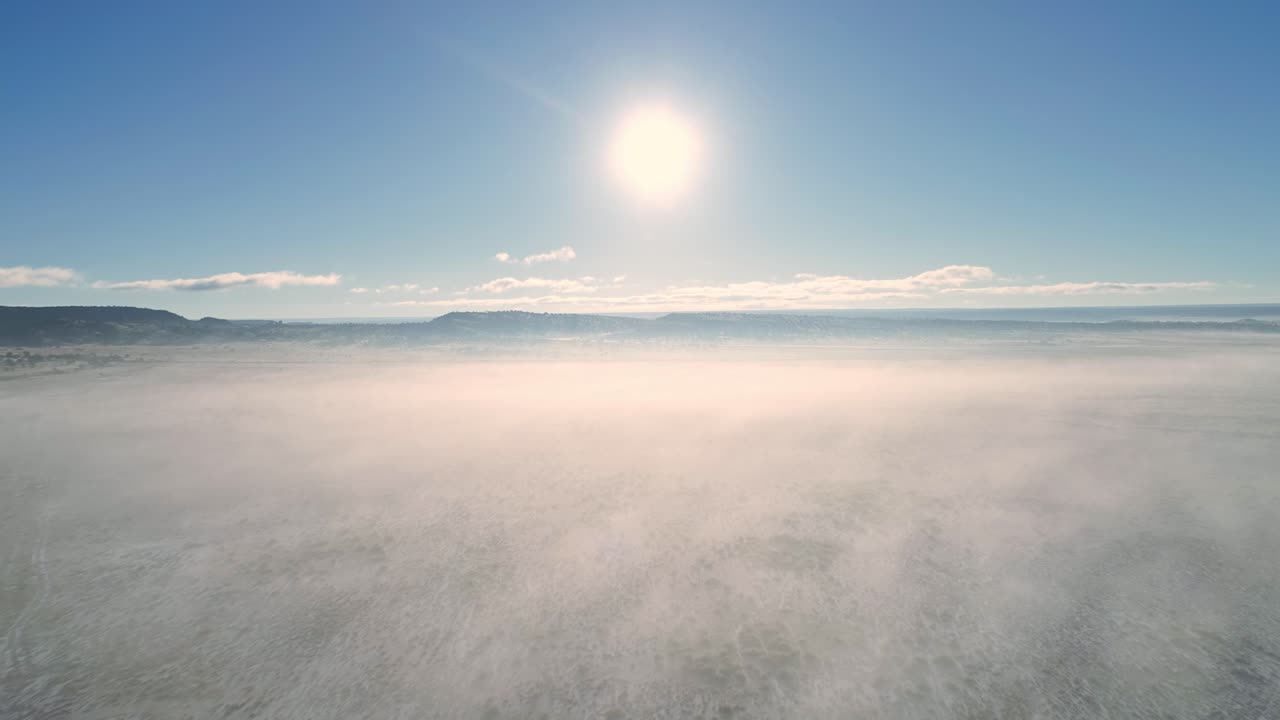 antena 4k sobre desierto nevado envuelto en niebla baja moviéndose hacia el sol naciente