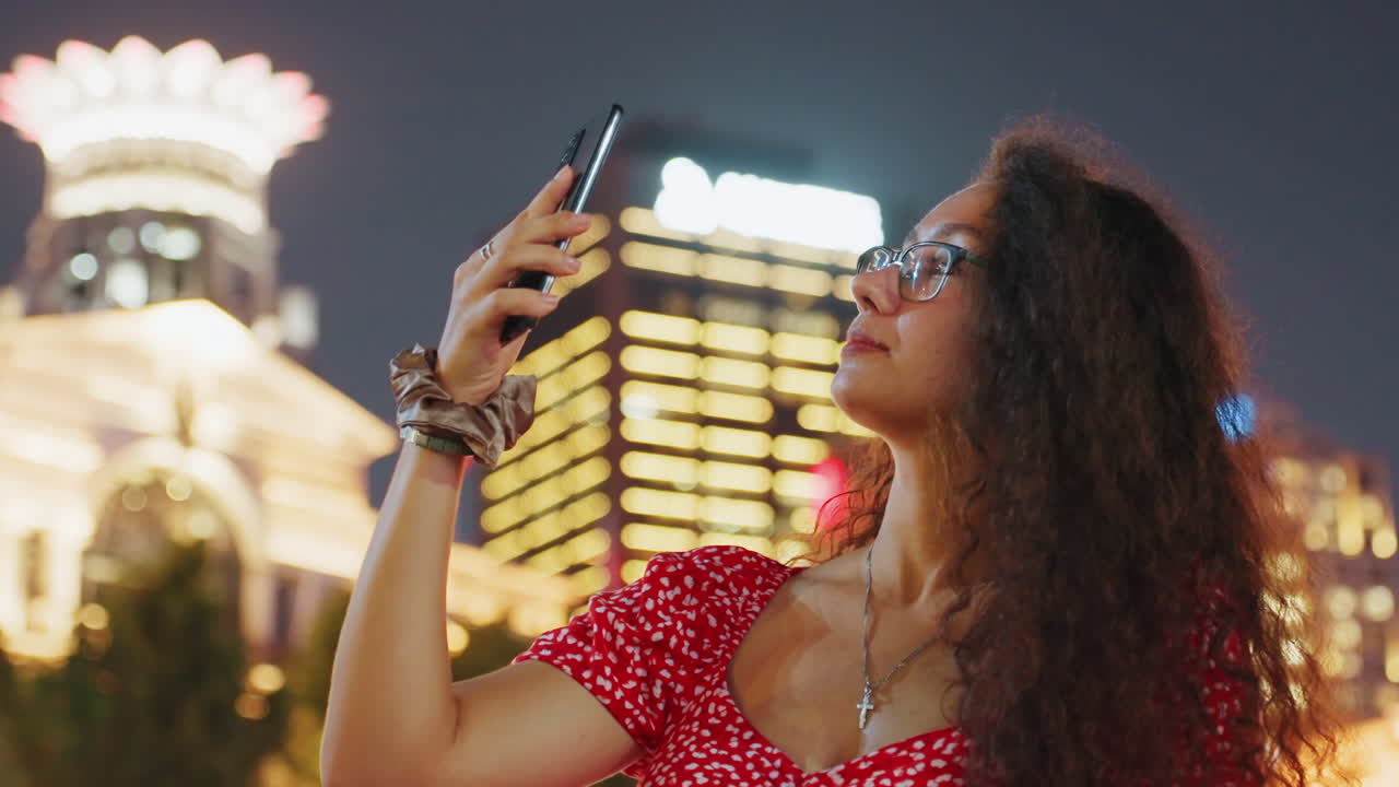 Horizonte noturno de néon, mulher negra verificando o telefone em close-up, óculos e vestido vermelho captando o brilho da cidade, rolando a tela do smartphone com fundo bokeh, criadora de conteúdo confiante capturando um momento urbano.