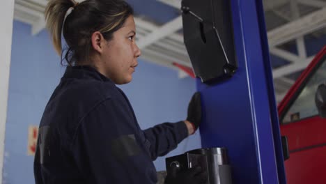 Mecánica-Femenina-Levantando-Un-Automóvil-Con-Una-Grúa-Automática-Presionando-Un-Botón-En-Una-Estación-De-Servicio-De-Automóviles