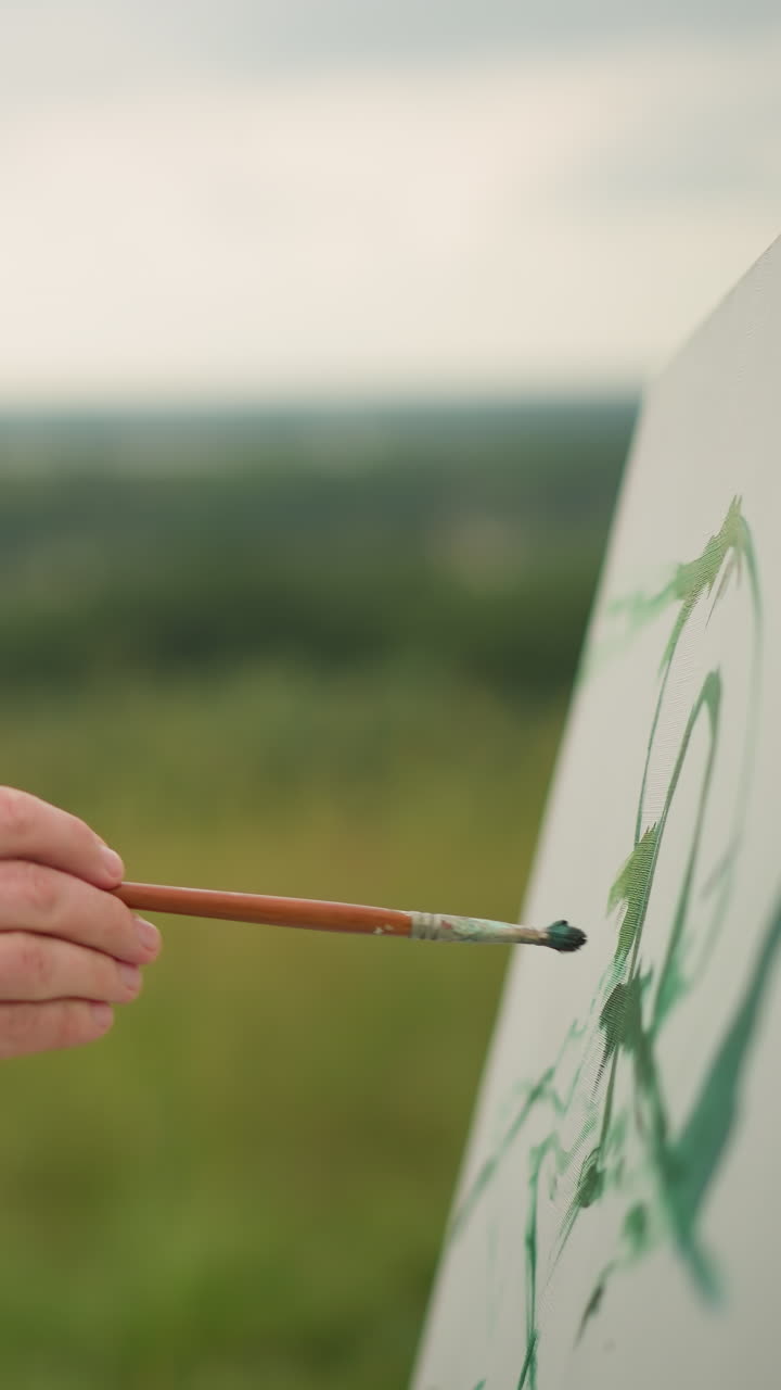 숙련된 공예가 한 손에는 페인트 팔레트, 다른 손에는 을 들고 큰  캔버스에 녹색 페인트를 부드럽게 칠하는 모습.