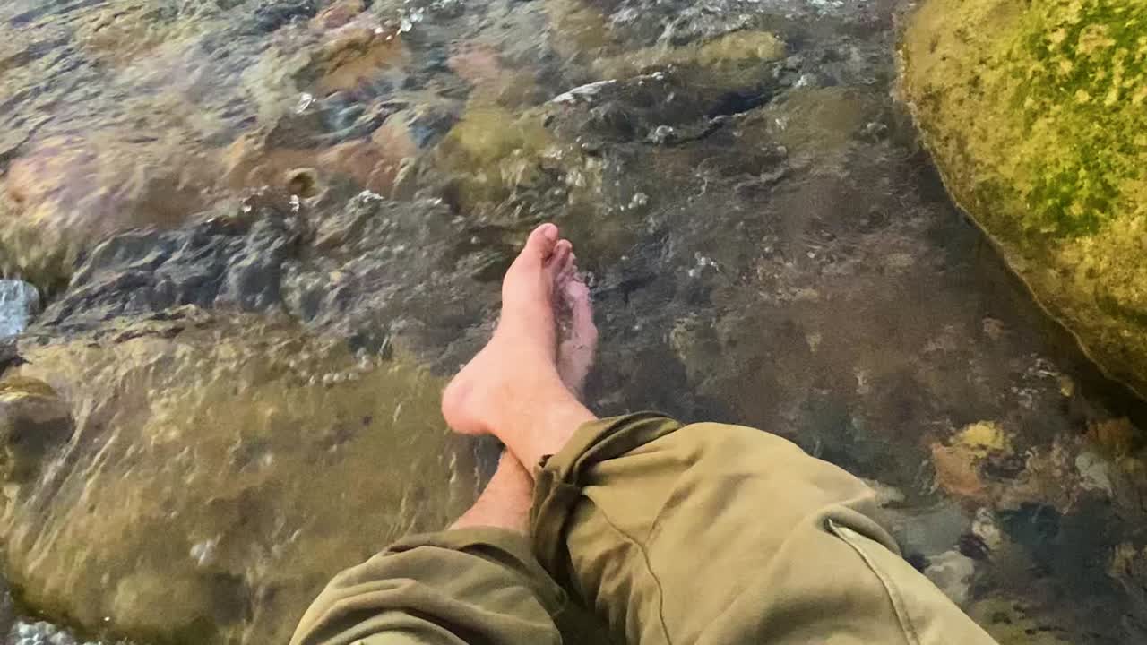Moment of relaxation with a person bare feet immersed in the clear cool water of a rocky river