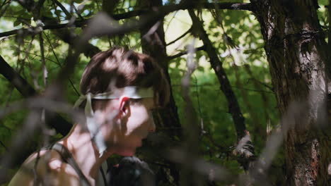 side view of soldier squeezing through dry branches while forcefully punching rough tree bark under dense green foliage, sweat-drenched arm gloved hand striking wood in intense outdoor training