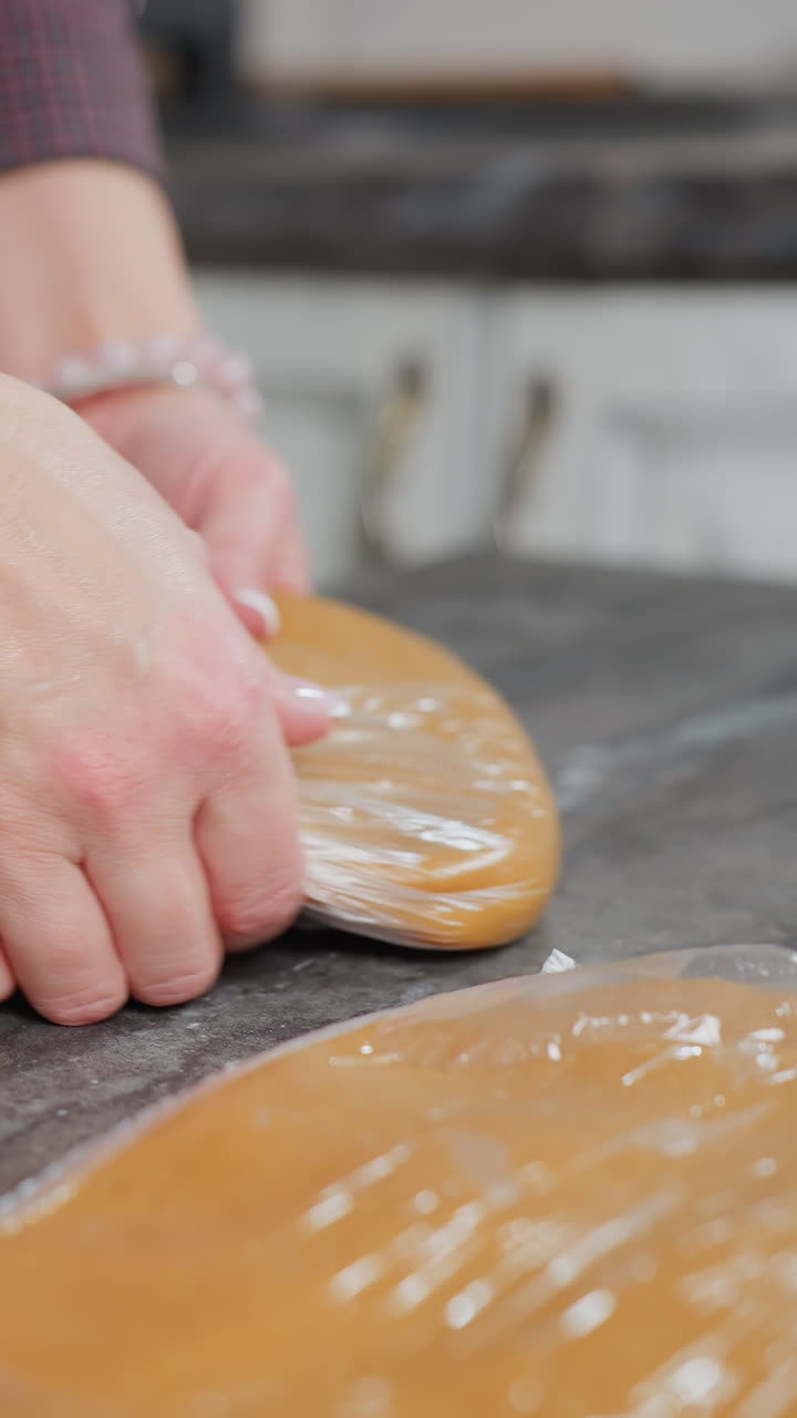 가죽으로 감싸진 반죽을 다른 반죽 위에 놓고, 손목으로 장식된 손으로, 현대 주방의 깨한 카운터에 베이킹 준비를 조심스럽게 준비하는 여성의 클로즈업