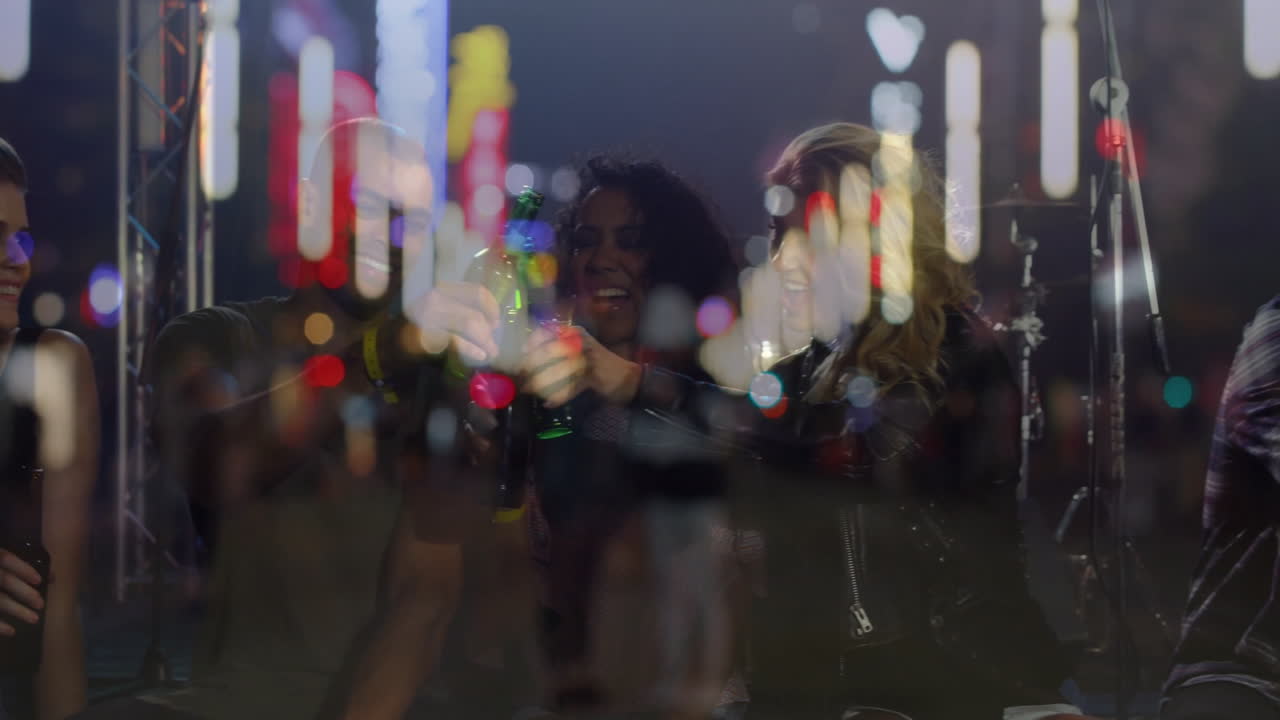 group of five friends clinking green bottles in music venue, showing animated mic stands and bokeh