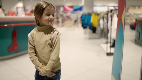 Little-girl-put-small-backpack-on-shoulders-looking-to-the-mirror-at-store