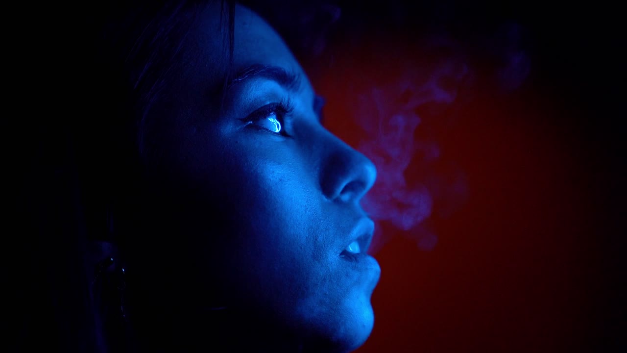 Young attractive woman smoke lit by blue light. Bad habits concept